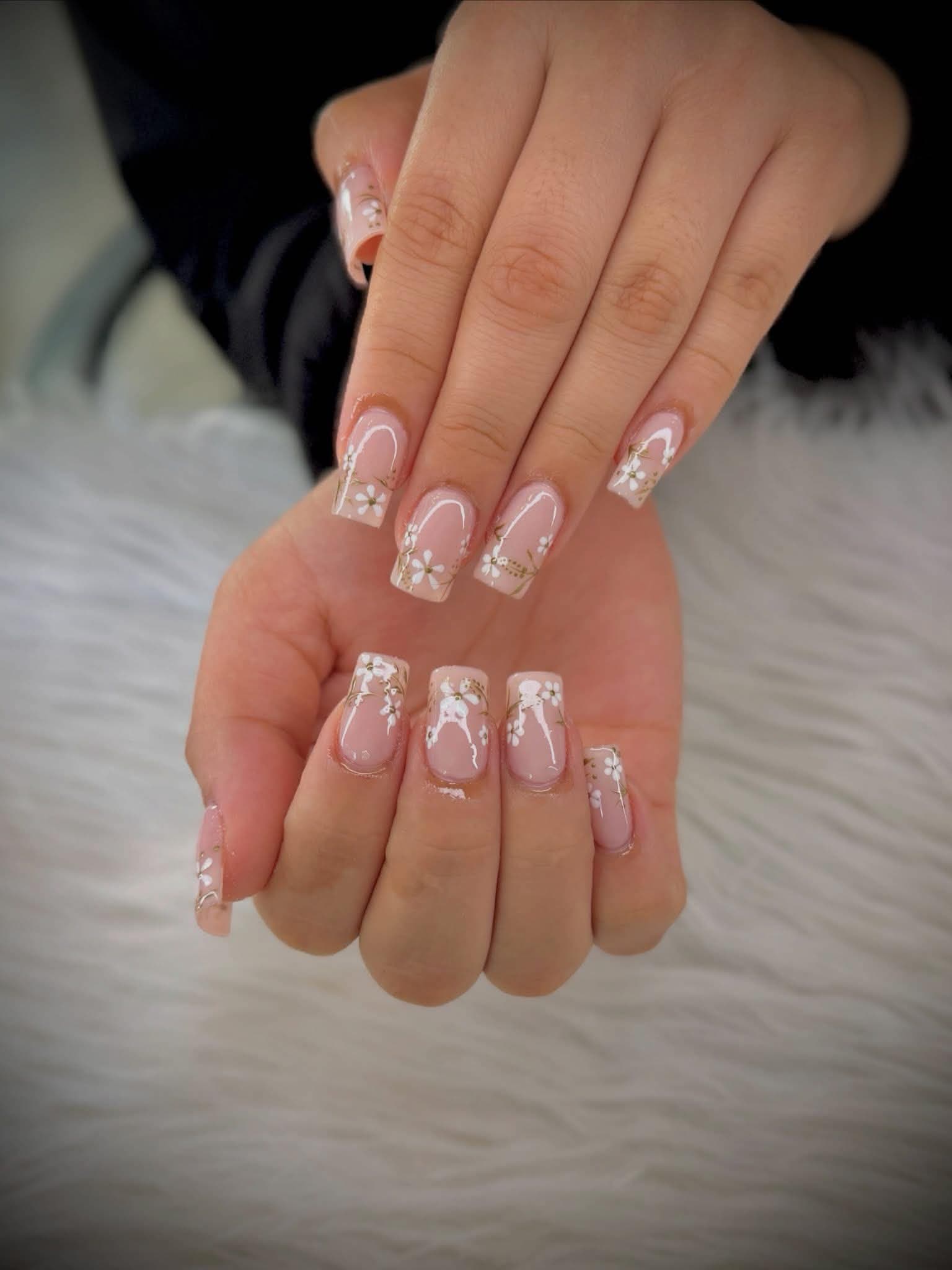 Square nude nails painted with fine white blossoms and gold stems